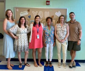 Third grade team poses with smiles in front of a bulletin board